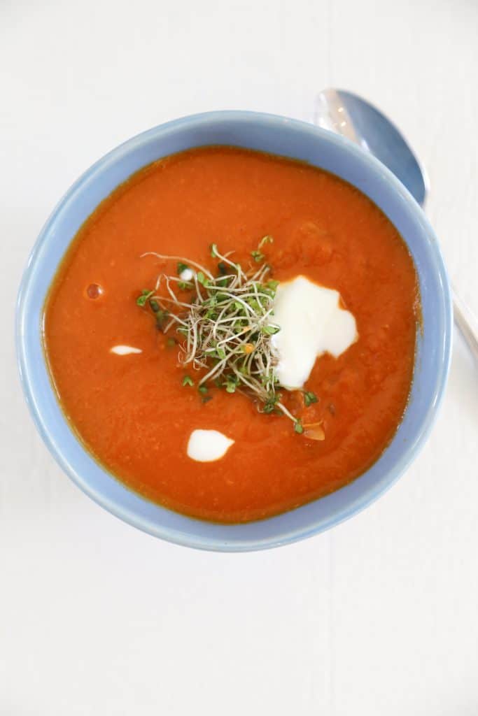 gluten free tomato soup in a blue bowl with microgreens