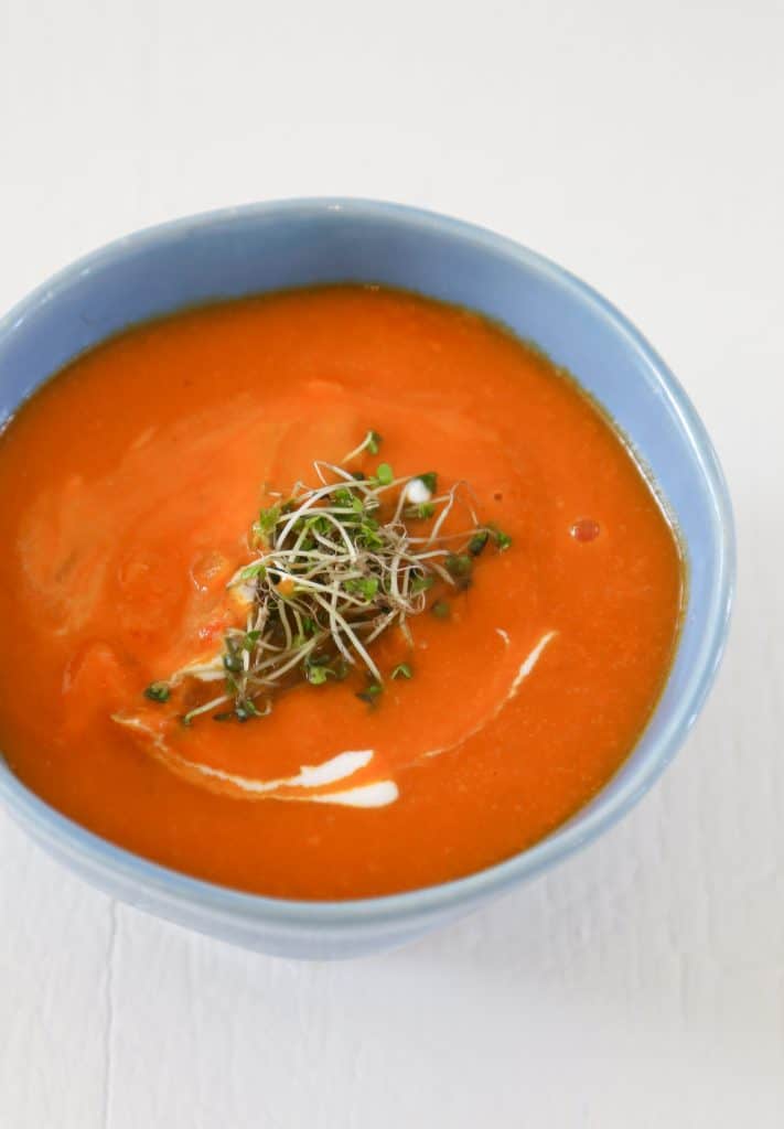 gluten free tomato soup in a blue bowl with sprouts 