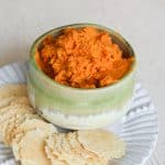 gluten free hummus with roasted carrots and Peruvian spice blend in a green bowl on a plate with crackers