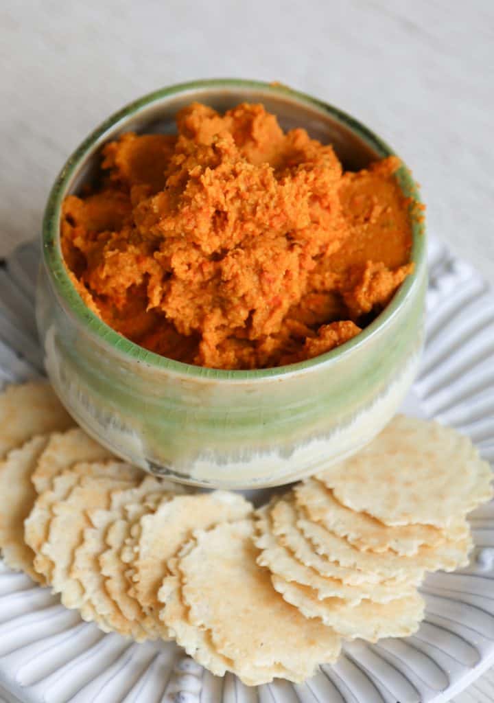 bowl of gluten free hummus with carrots in a green bowl with crackers on a white plate.