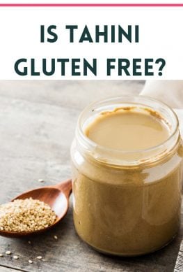 image of tahini in a glass jar next to a wooden spoon with sesame seeds that says is tahini gluten free?