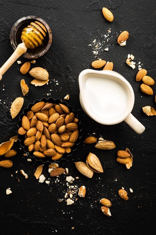 photo of almond milk, almonds and honey on a black table 