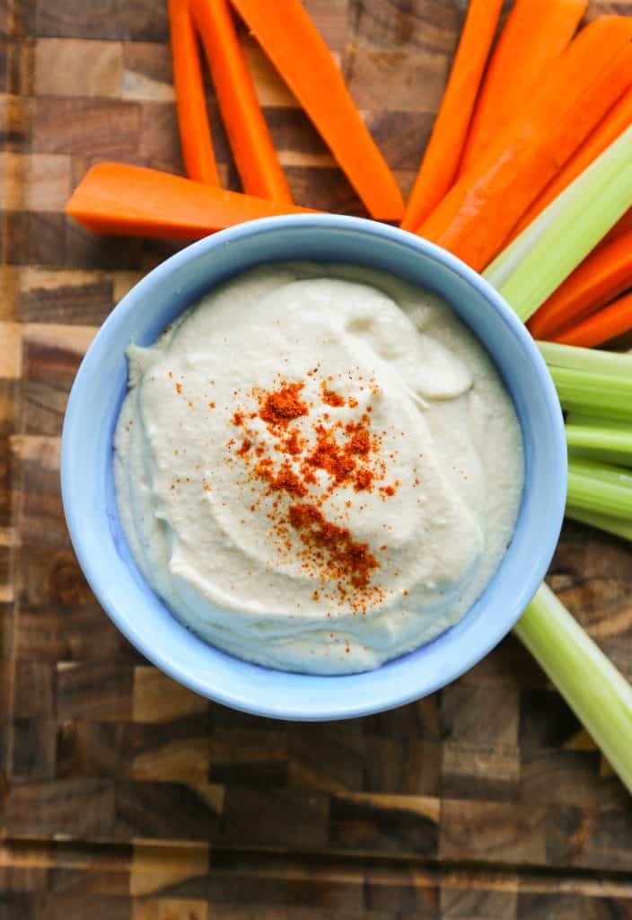 photo of vegan garlic aioli (mayo) in a blue plate on a cutting board surrounded by vegetables.