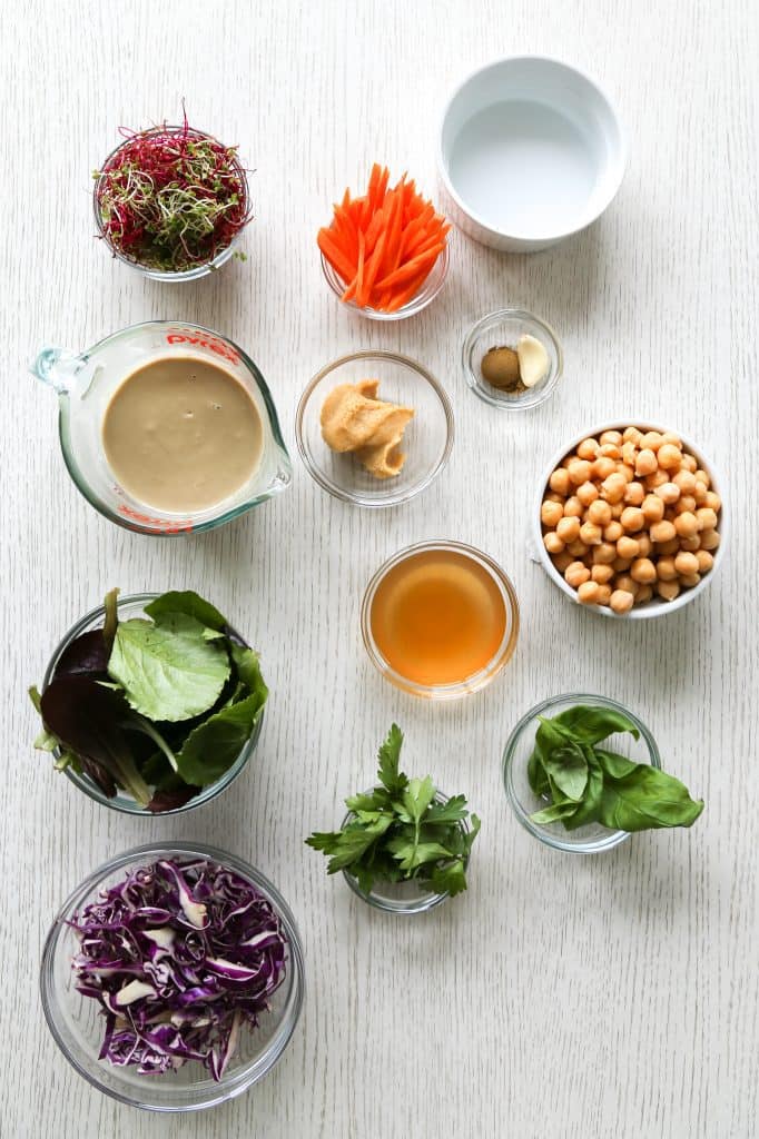 ingredients for microgreen salad, microgreens, carrots, water, tahini, miso paste, garlic, chickpeas, vinegar, salad greens, parsley, basil, purple cabbage.