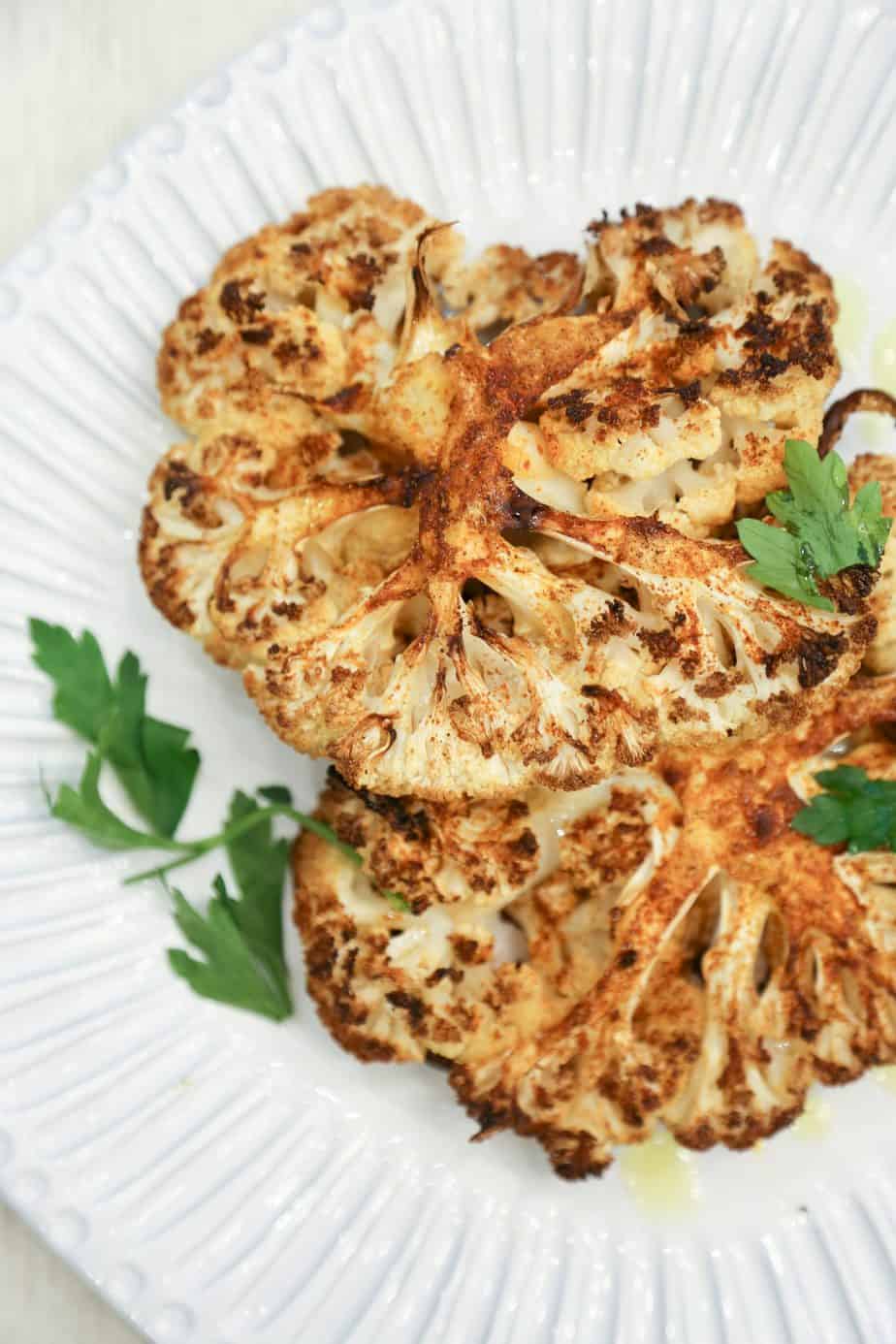 Air fryer cauliflower steaks made with Peruvian spice blend on a white plate garnished with parsley and olive oil.