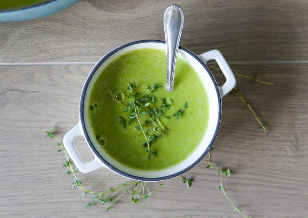 photo of vegan pea soup in a white bowl with a spoon garnished with thyme