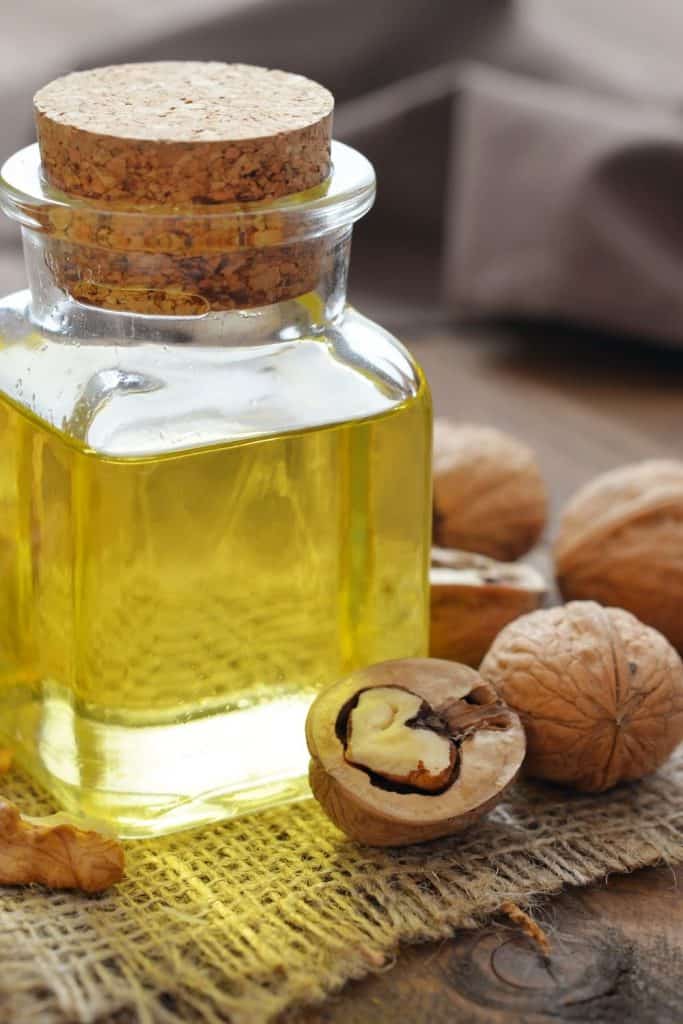 walnuts on a table next to a glass container of walnut oil