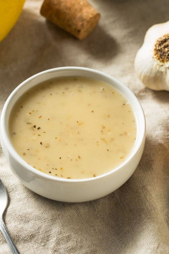 oregano vinaigrette in a white bowl on a table with garlic lemon and a cork