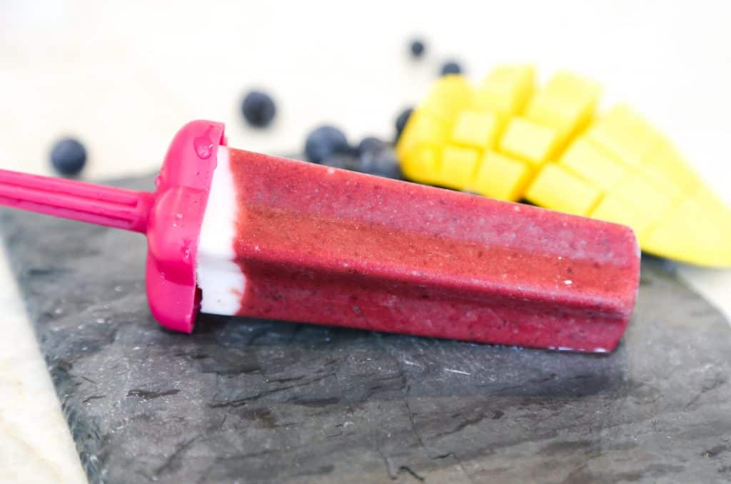 one cherry popsicle with mangos and blueberries in the background