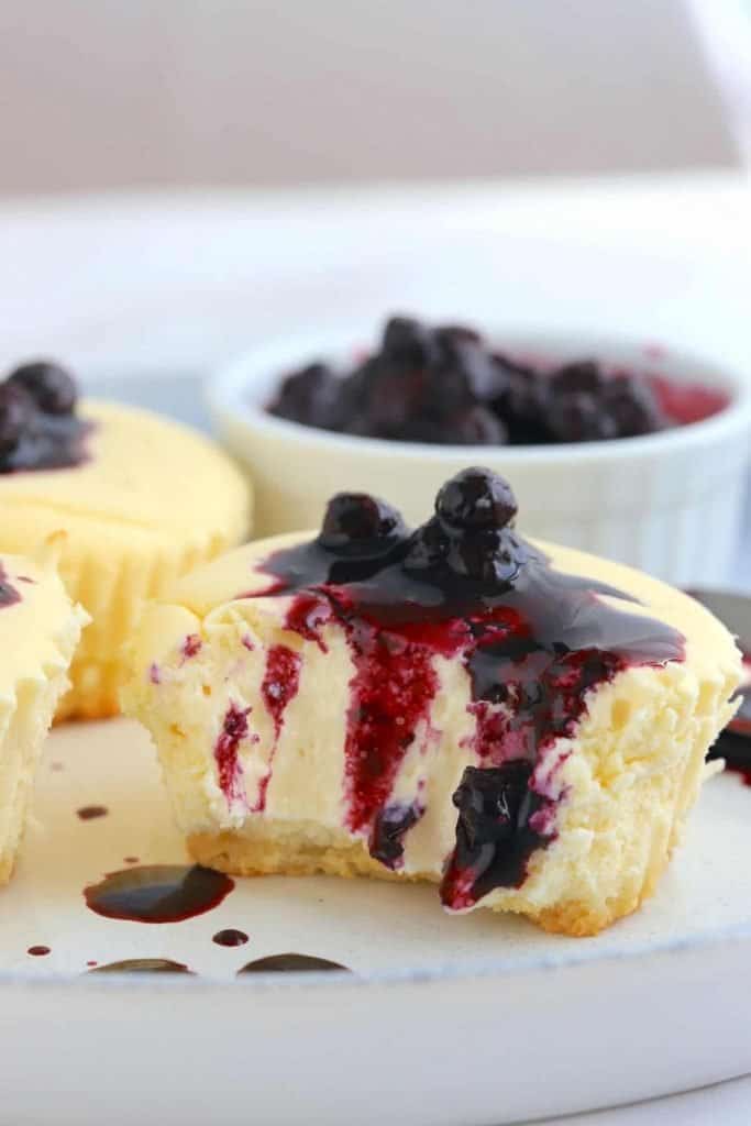 Keto Cheesecake Cupcakes are a sugar free, creamy and delicious guilt free dessert that is super rich, light and airy. on a plate cut open with blueberries dripping down
