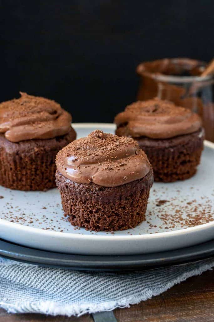 vegan and gluten free chocolate cupcakes on a plate with chocolate powdered sugar and frosting