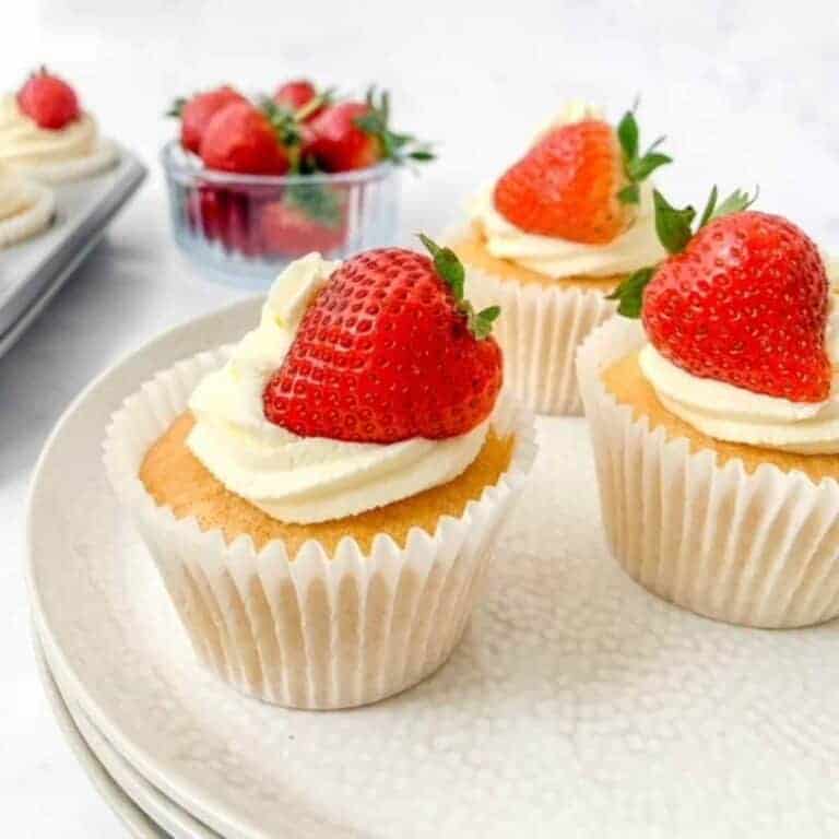 victoria sponge cake cupcakes with strawberries on top on a plate.