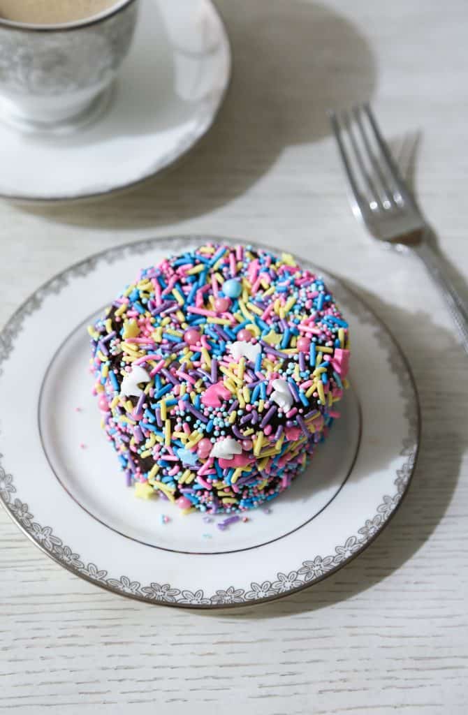 gluten free bento cake covered in sprinkles on a cake plate with fork and a cup of coffee.