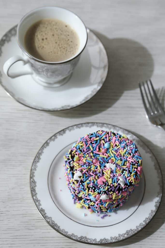 gluten free bento cake covered in sprinkles on a cake plate with fork and a cup of coffee.