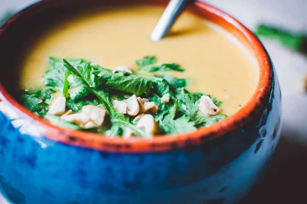 gluten free cashew and carrot soup in a bowl with leaves and nuts 