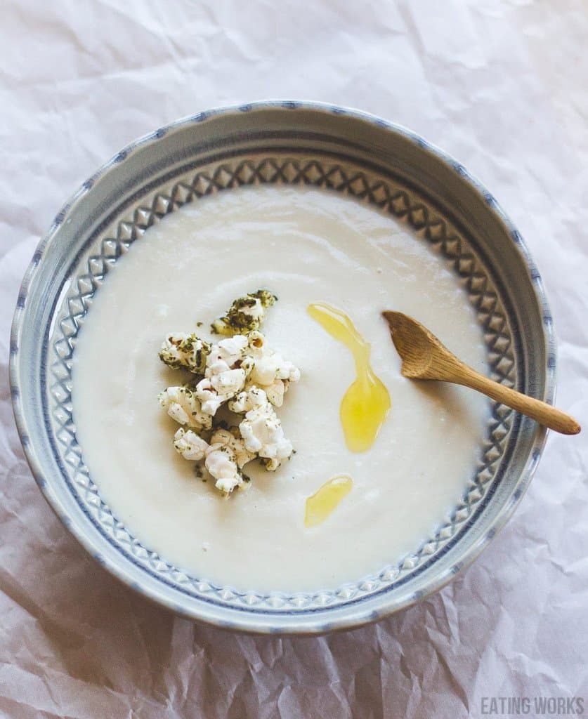 gluten free cauliflower soup in a bowl with cauliflower and olive oil drizzle and a wooden spoon