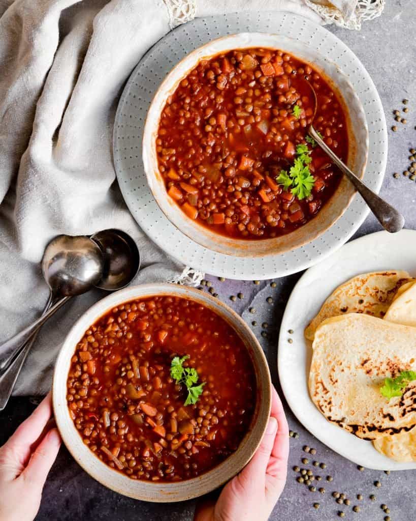 two bowls of vegan red chili with bread and spoons 