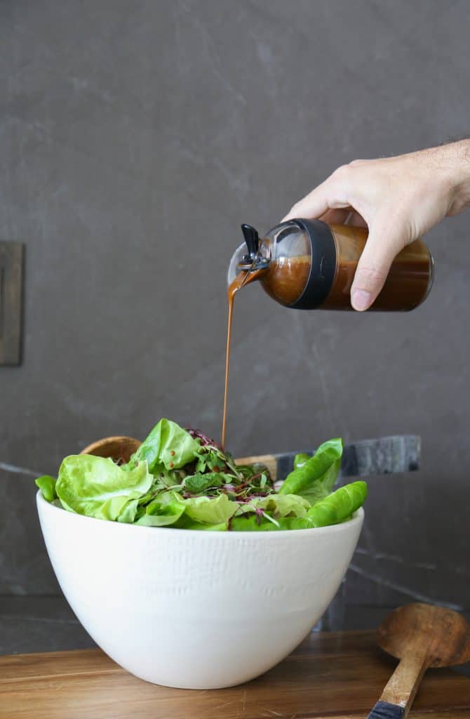 creamy balsamic dressing being poured into a large green salad in a white bowl