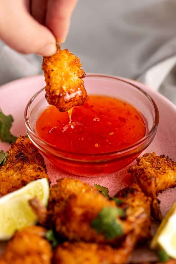 air fryer coconut shrimp in hand being dipped into red sauce