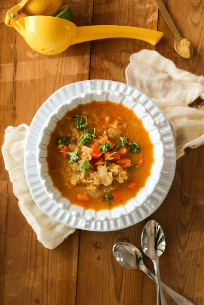 bowl of moroccan red lentil soup with two spoons and a citrus juicer 