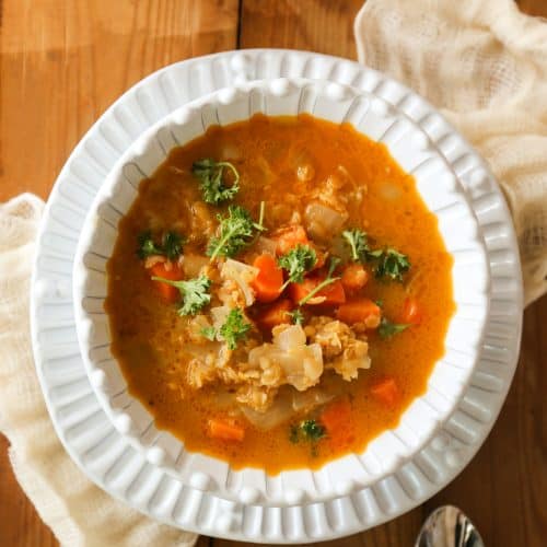 Moroccan red lentil soup in a bowl with two spoons and a citrus juicer