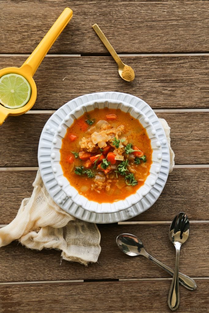 bowl of moroccan red lentil soup with two spoons and a citrus juicer 