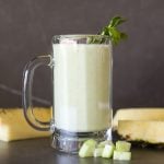 pineapple cucumber smoothie in a glass with chopped cucumber chunks and wedges of pineapple garnish