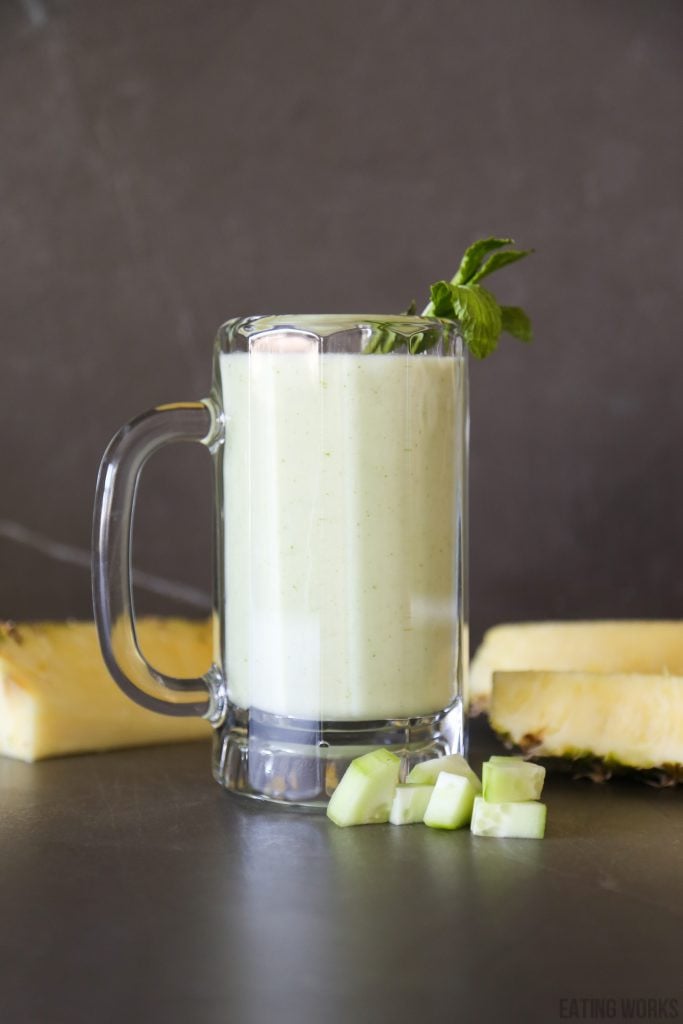 pineapple cucumber smoothie in a glass with chopped cucumber chunks and wedges of pineapple garnish