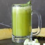 Cucumber and pineapple juice in a glass with sliced cucumber and cilantro garnish