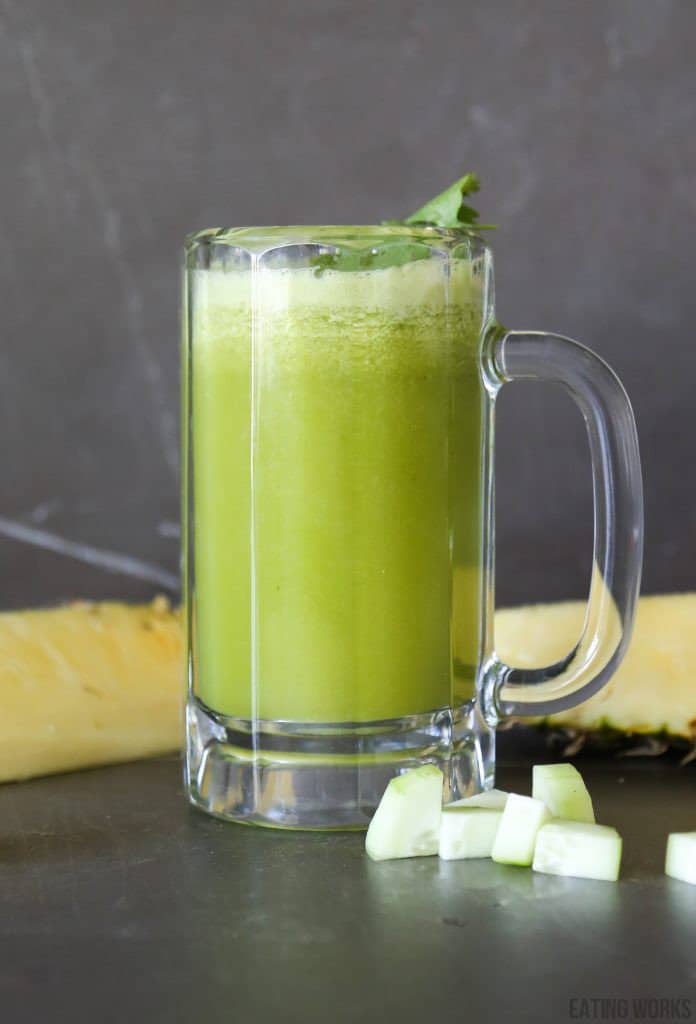 Cucumber and pineapple juice in a glass with sliced cucumber and cilantro garnish