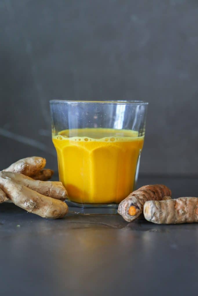 glass filled with lemon ginger turmeric shot with ginger and turmeric roots 