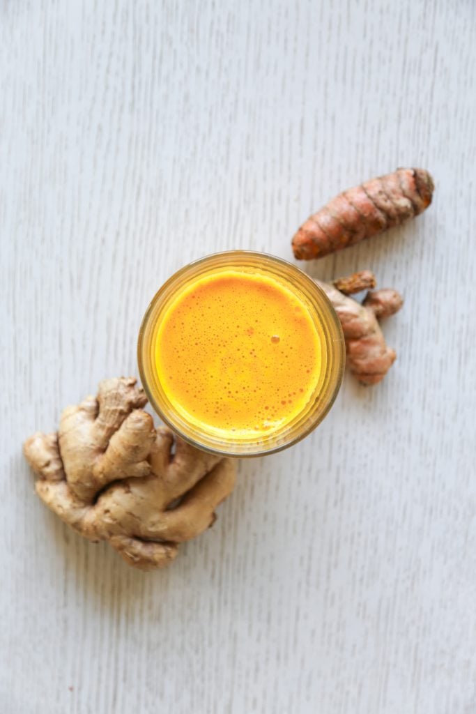 glass filled with lemon ginger turmeric shot with ginger and turmeric roots  from above 