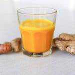 glass filled with lemon ginger turmeric shot with ginger and turmeric roots