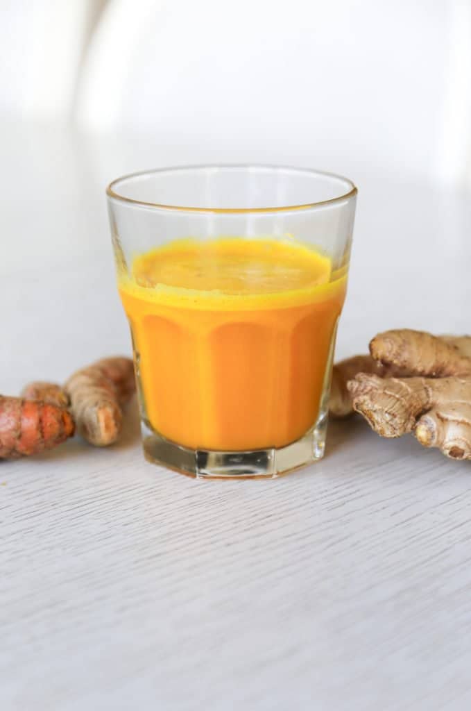 glass filled with lemon ginger turmeric shot with ginger and turmeric roots 