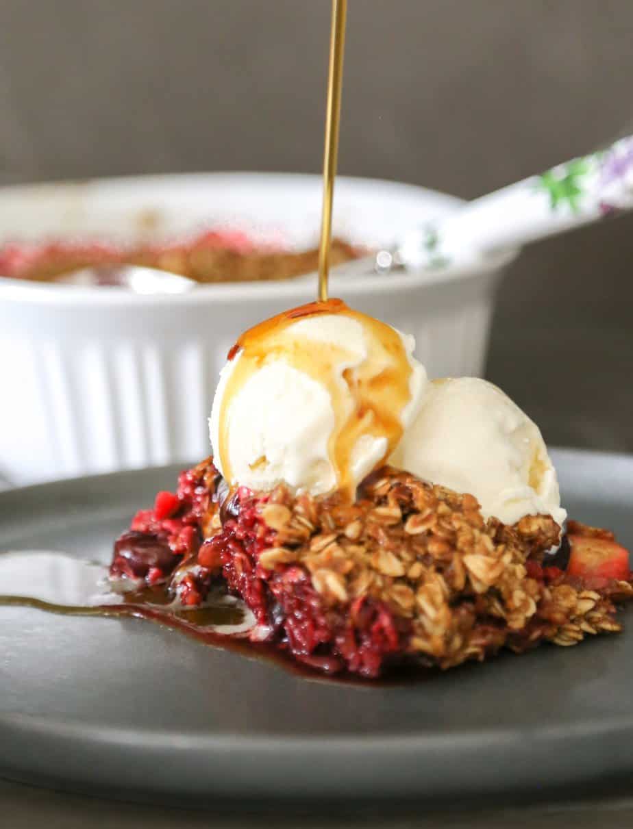 Apple and berry cobbler with vanilla ice cream and sauce drizzled on top.