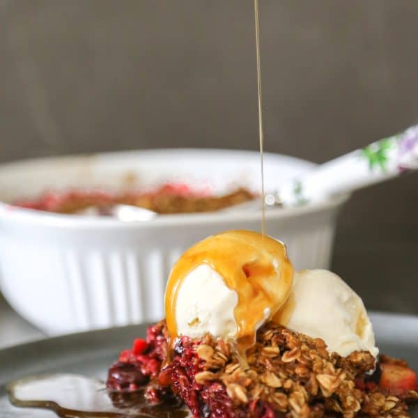 apple and berry cobbler on a plate with ice cream and sauce drizzled on top