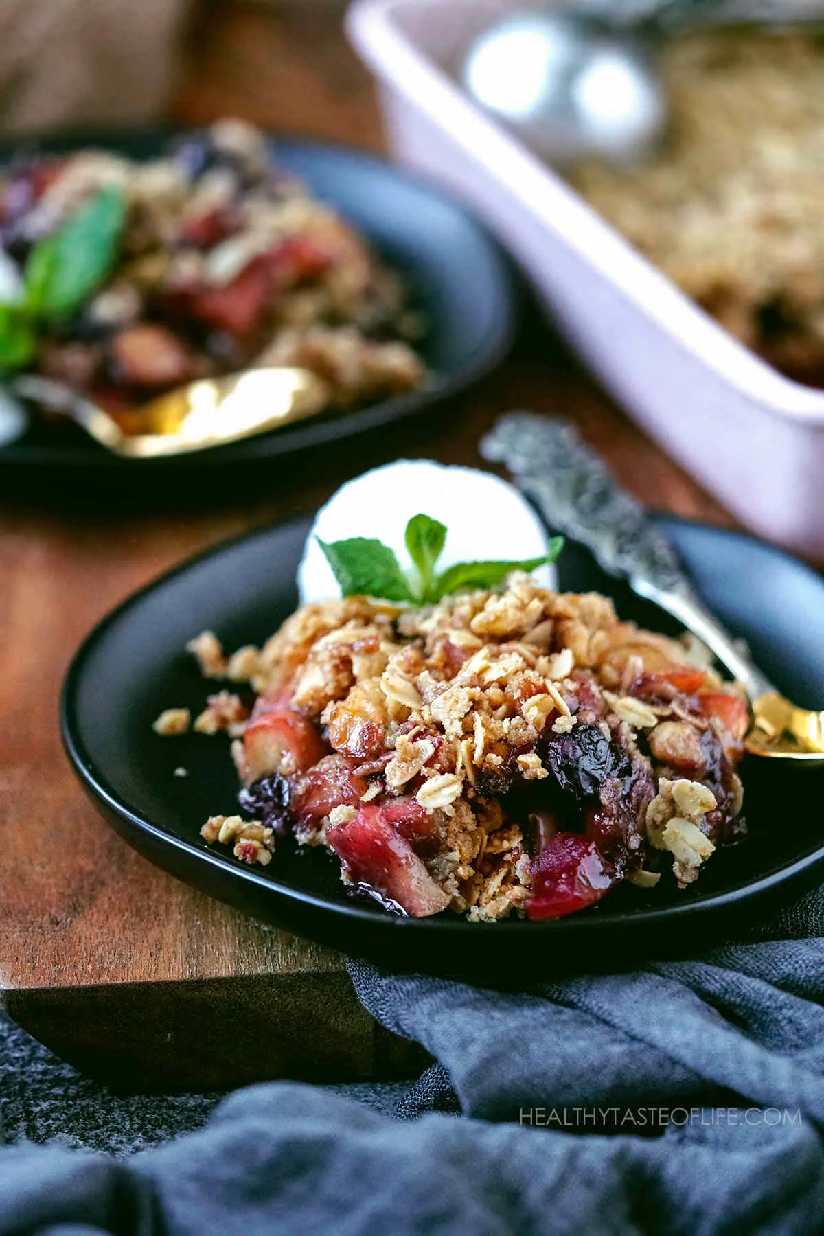 Warm apple and blueberry crumble on a plate served with a scoop of ice cream.