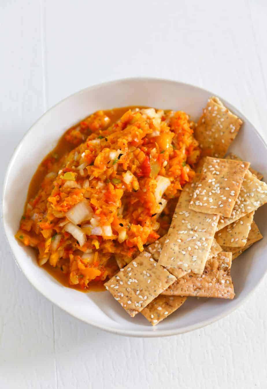 Photo of roasted  pepper salsa in a white bowl with crackers. Dips for charcuterie board.