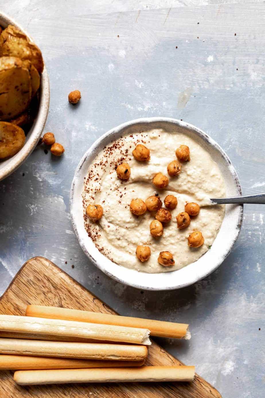 A bowl of hummus with roasted chickpeas on top. Dips for charcuterie boards.