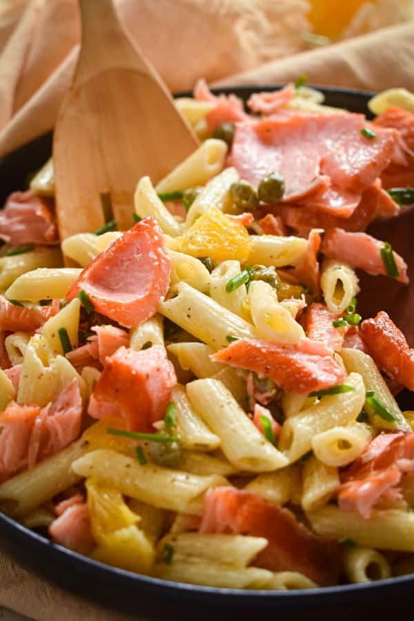 Smoked salmon pasta salad in dish with wooden spoon.