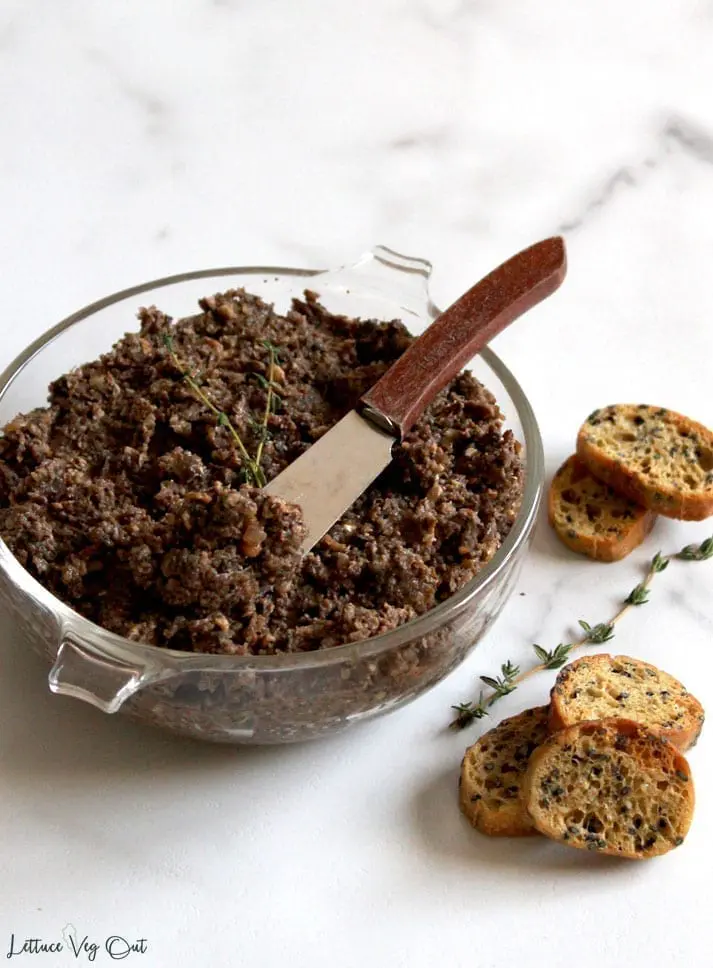 Vegan mushroom pate recipe in a glass bowl with small baguette crisps ready to scoop and serve.