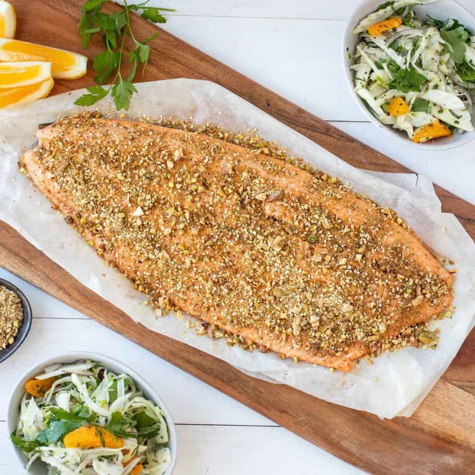 Baked salmon fillet with dukkah crumb on wooden board.