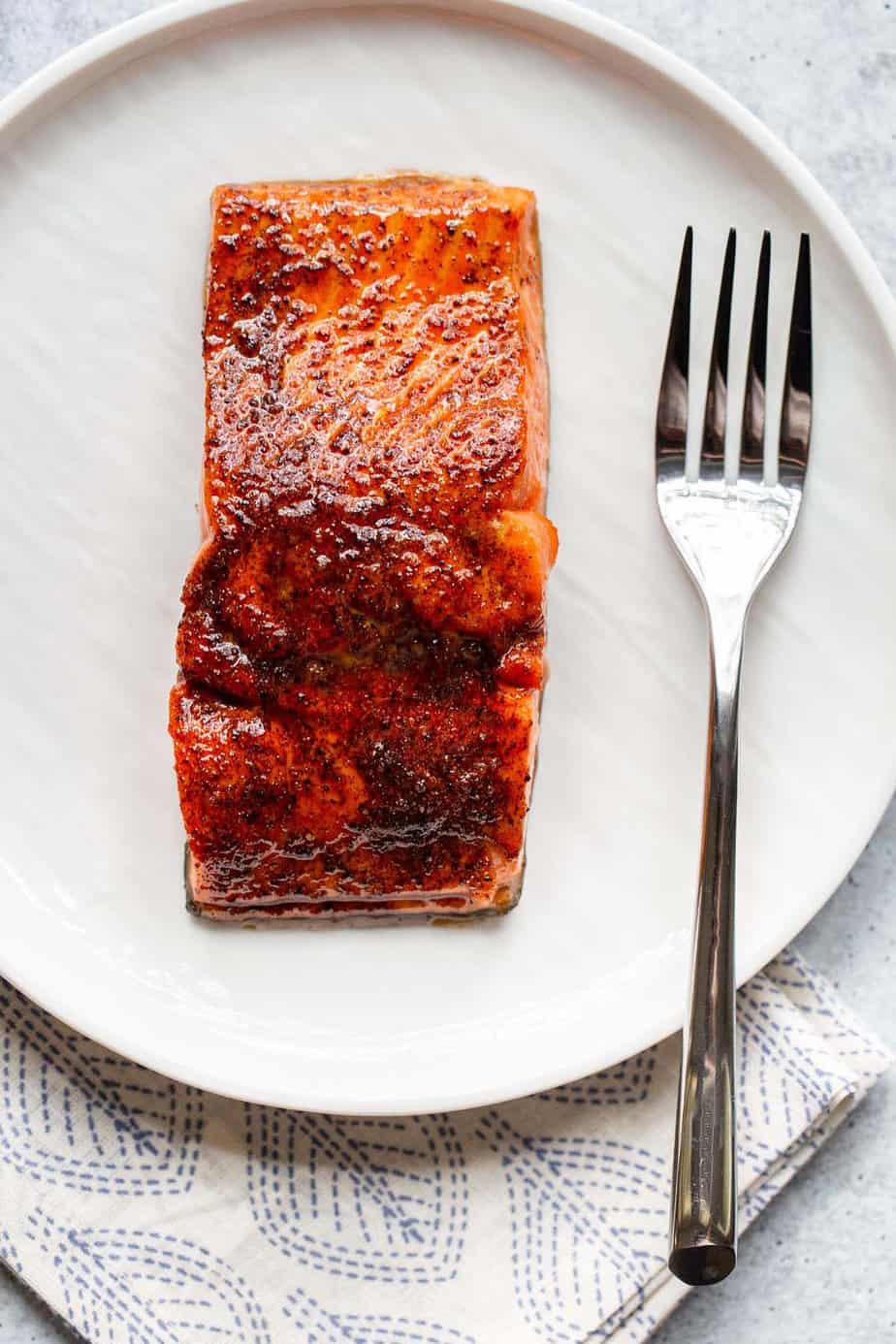 Cooked salmon on a white plate with a fork.