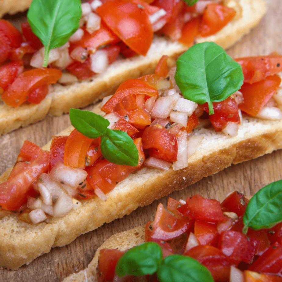 A close up of four slices of bruschetta   topped with extra tomatoes and basil.